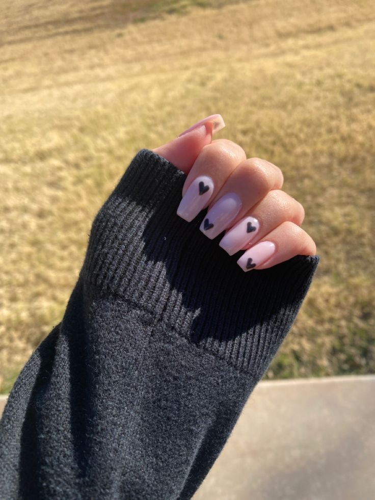 Chic Nude Base Nail Design with Bold Black Heart Accents for a Modern Whimsical Look.