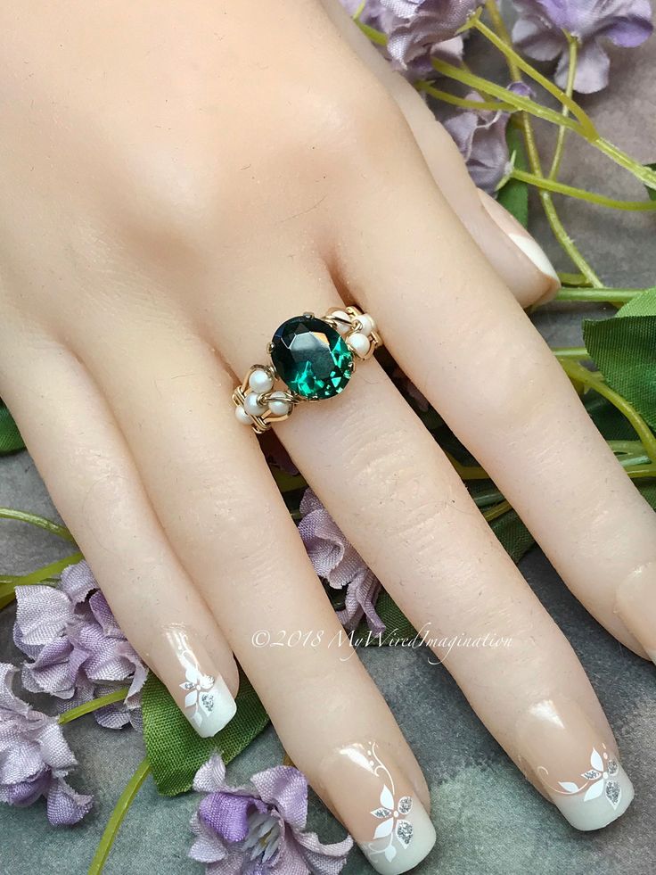 Sophisticated Nude Nail Design with Floral Accents and Emerald Stone Ring.