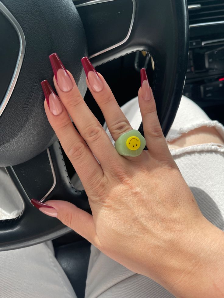 Chic Almond-Shaped Burgundy Tip Nails with Nude Base Paired with a Playful Statement Ring.