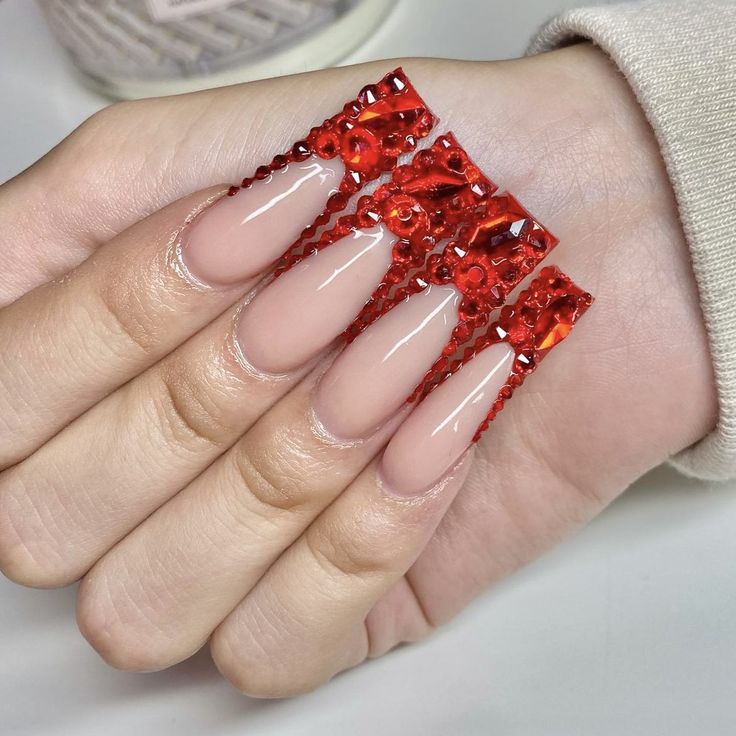 Chic Nude Nail Design with Striking Red Embellishments and Glamorous Gem Details.