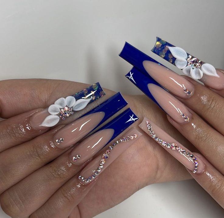 Elegant Blue and Nude Nail Design with Floral Accents and Rhinestones.