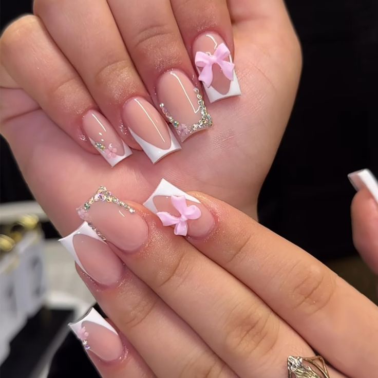 Elegant Chic Nail Design: Classic White Tips, Soft Pink Base, Delicate Bows, and Sparkling Gemstones.