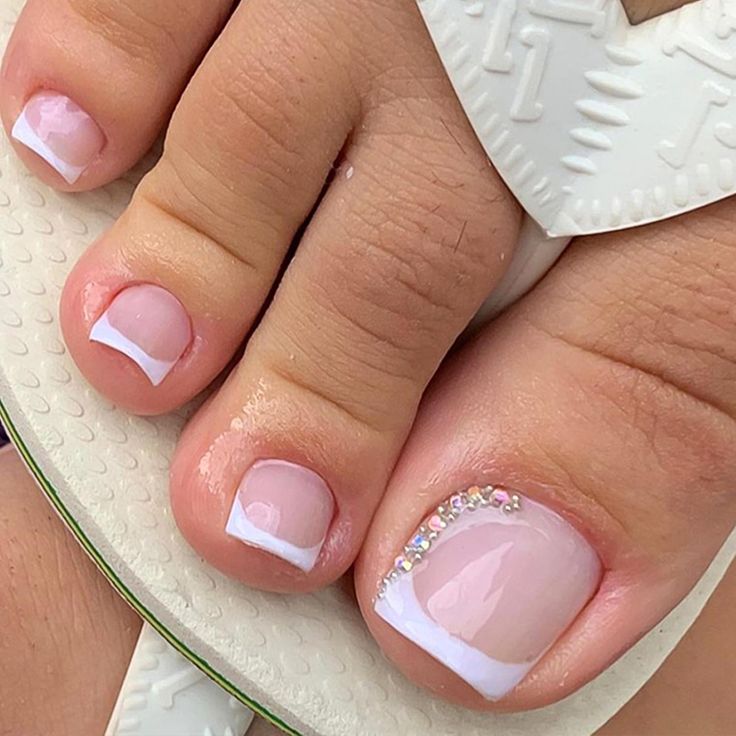 Elegant Sheer Pink Toenails with French Tips and Subtle Gemstone Accents for Summer Chic.