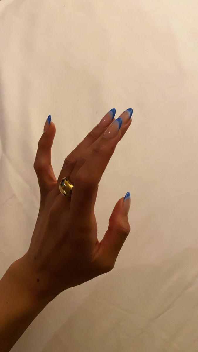 Chic Nail Art: Sophisticated Nude and Vibrant Blue Tips with Elongated Shape and Gold Ring Accents.