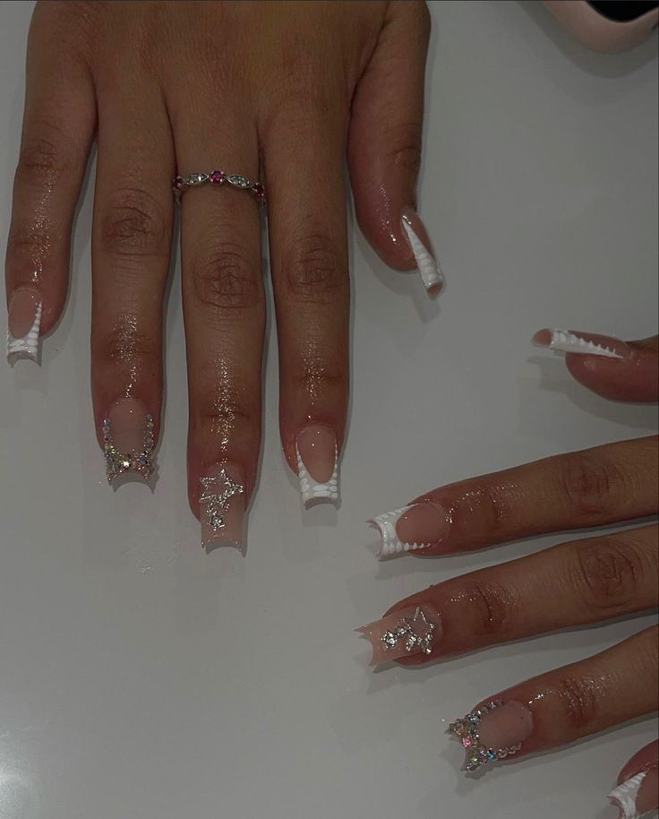 Elegant Nail Design: Long Square Tips with Intricate White Detailing and Glamorous Embellishments.