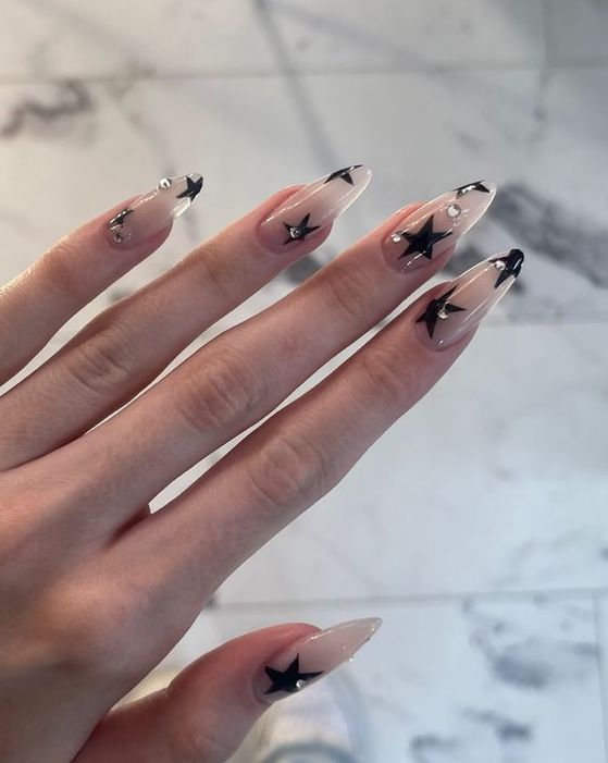 Chic Elegant Stiletto Nails: Nude Base, Glossy Black Tips, Star Motifs, and Rhinestones.