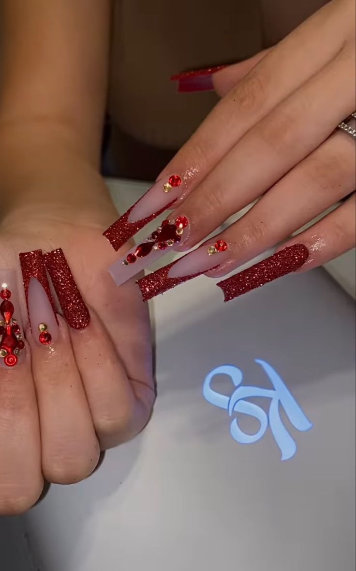 Glamorous Nail Design: Sparkling Red Glitter and Elegant Nude Tips with Vibrant Embellishments.