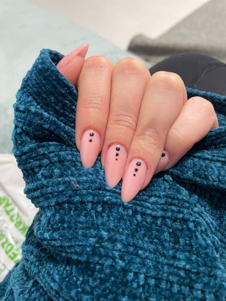 Chic Pastel Pink Almond Nails with Minimalist Black Dots Against a Cozy Teal Background.