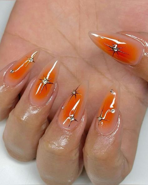 Playful and Sophisticated Summer Nail Design: Gradient Orange with Stiletto Shapes Adorned in Black Lines and Rhinestones.