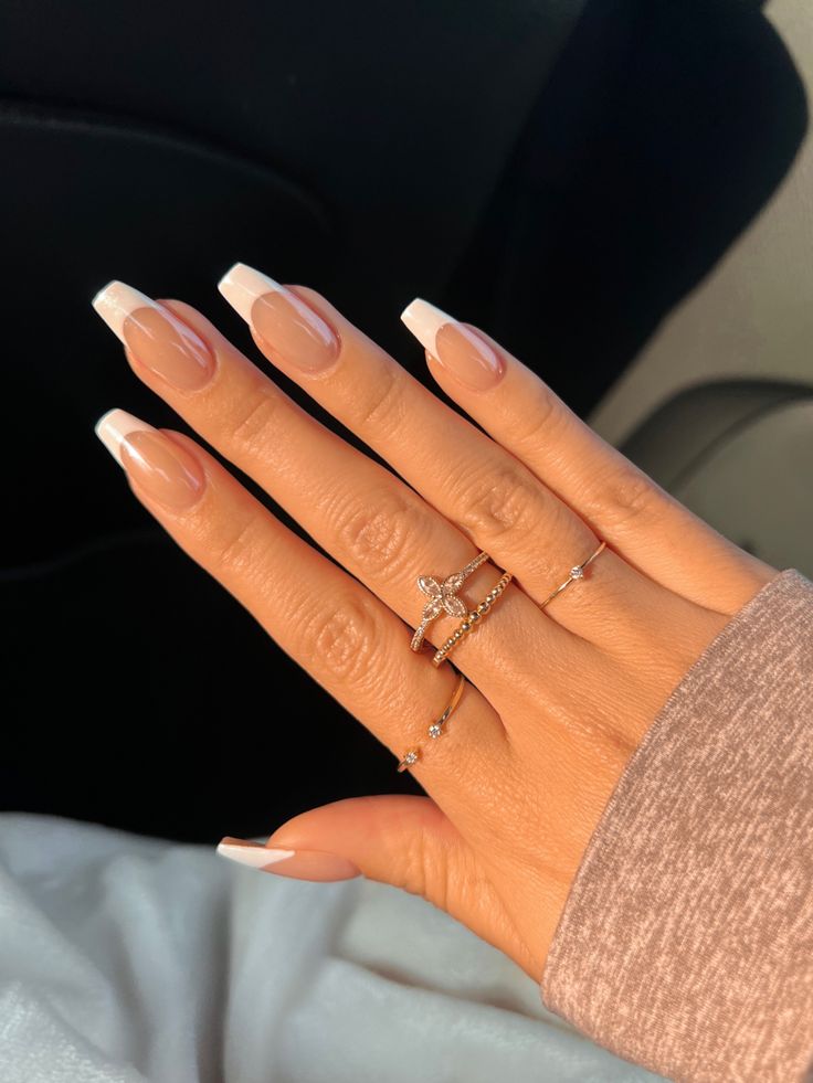 Chic Almond-Shaped French Tip Manicure with Elegant Nude Base and Delicate Rings.