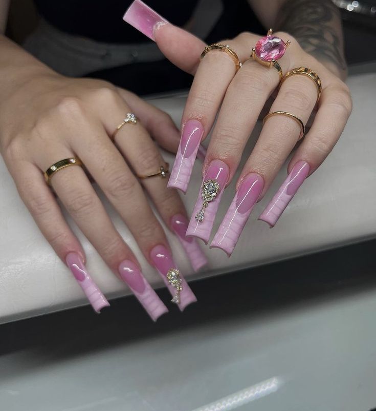 Elegant Gradient Pink Long Nails with Glamorous Embellishments and Gold Rings.