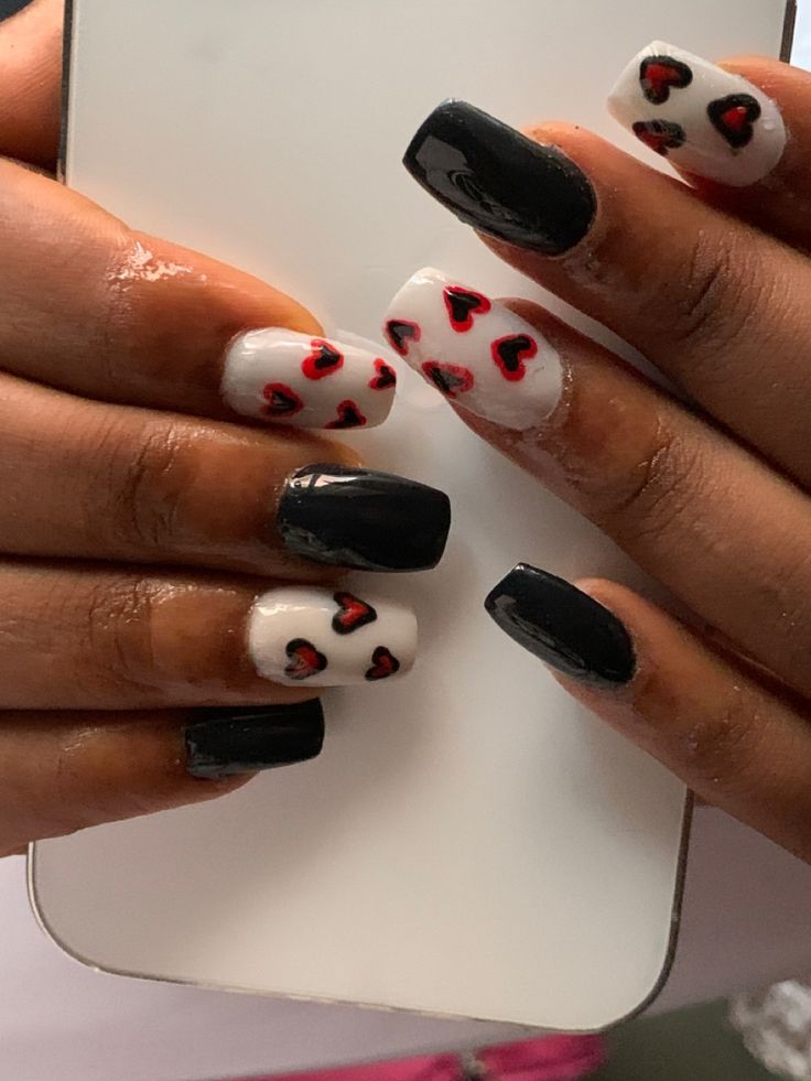 Playful Chic Nail Design: Glossy Black and Soft White with Vibrant Red Hearts.