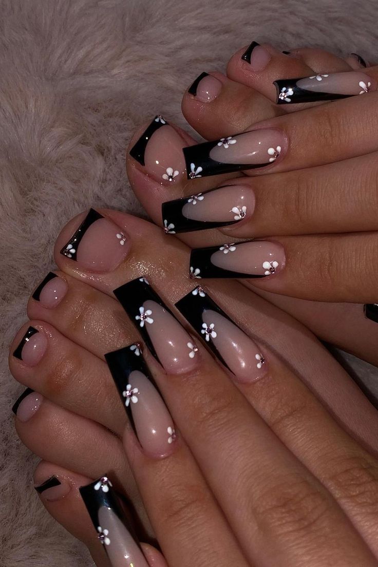 Modern French Tip Nail Design: Striking Black Tips with Delicate White Flowers on Nude Base.