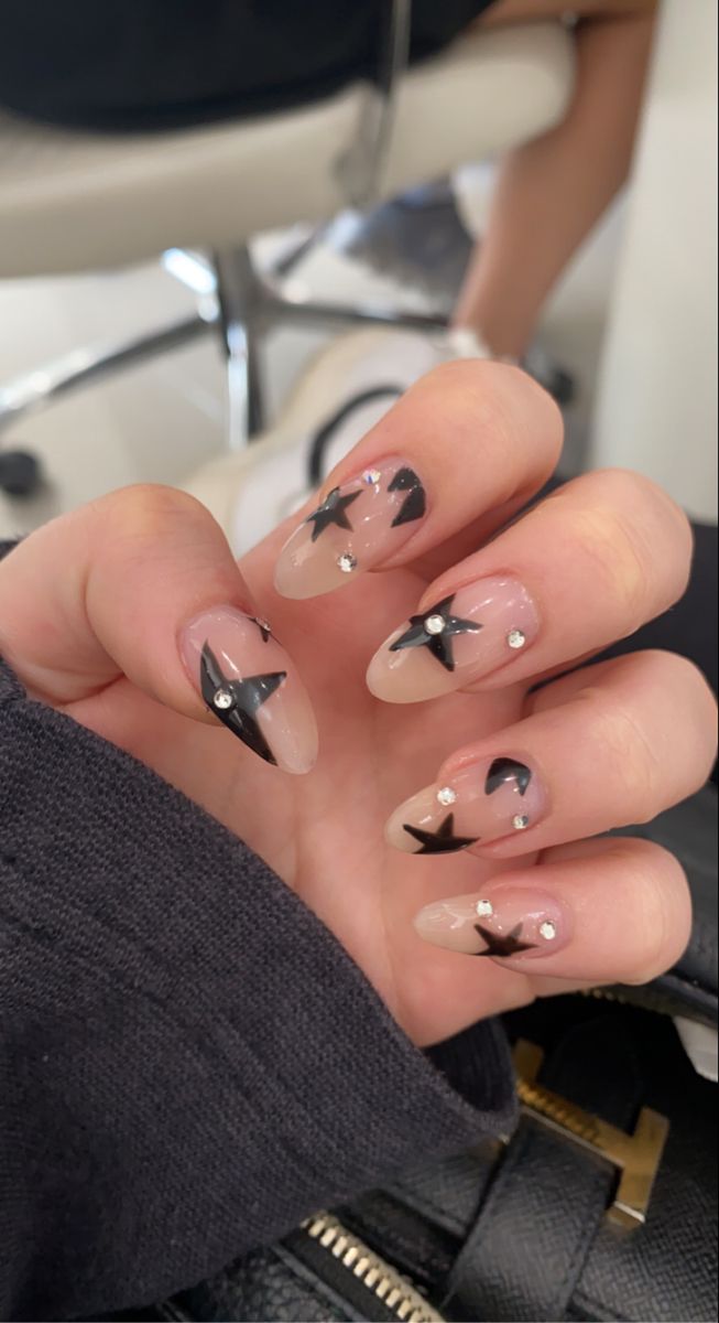 Playful Retro Nail Design: Nude and Translucent Bases with Bold Black Stars and Sparkling Rhinestones.