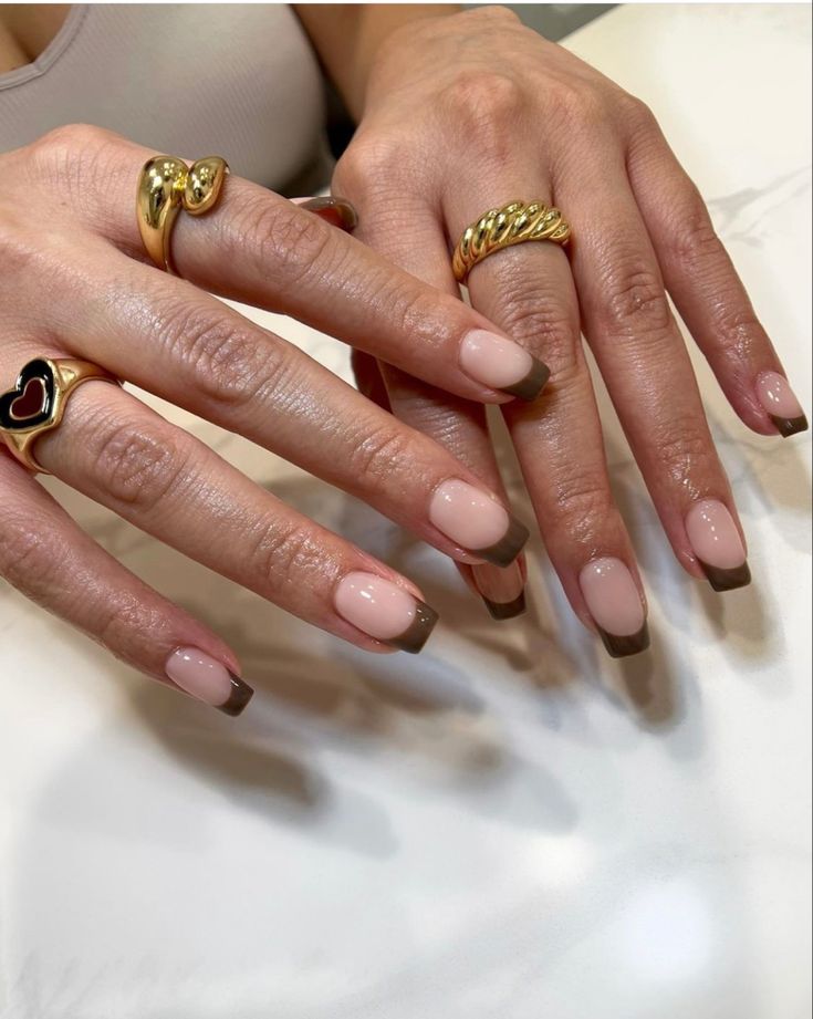 Chic French Tip Nails with Nude Base and Brown Tips, Accentuated by Elegant Rings.