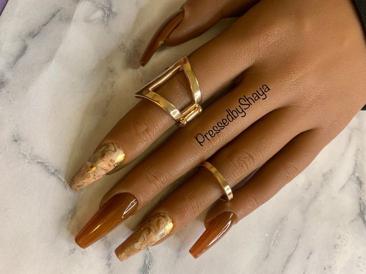 Chic Almond-Shaped Nails in Warm Brown Tones with Gold Accents and Minimalist Rings.