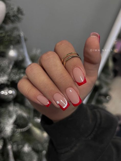 Chic French Tip Manicure with Striking Red Tips and Delicate Rings.