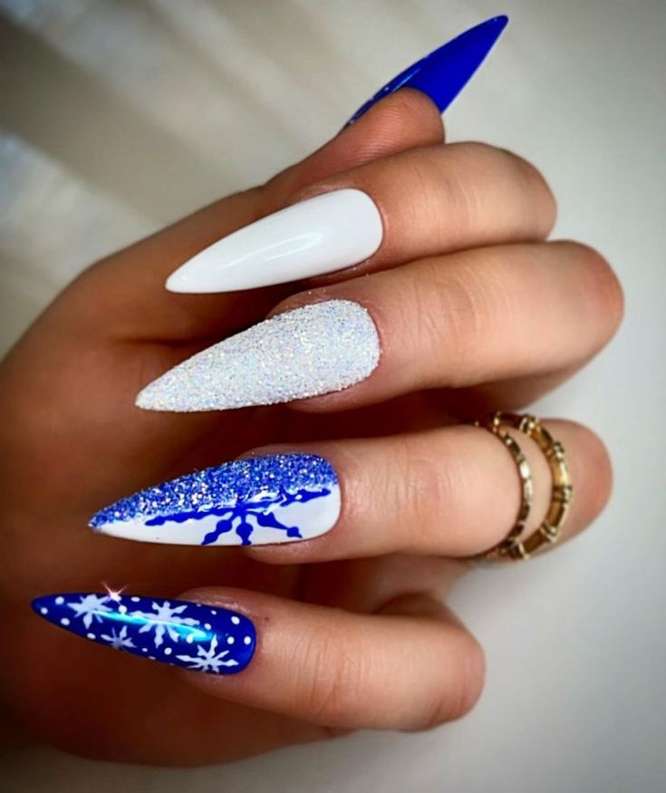 Elegant Winter-Inspired Stiletto Nail Design with Glossy White, Royal Blue, and Glitter Snowflake Patterns.