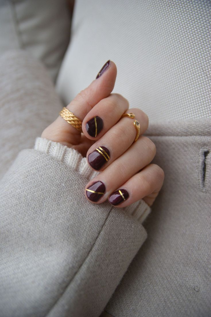 Chic Deep Burgundy Nail Design with Elegant Gold Accents and Geometric Lines.