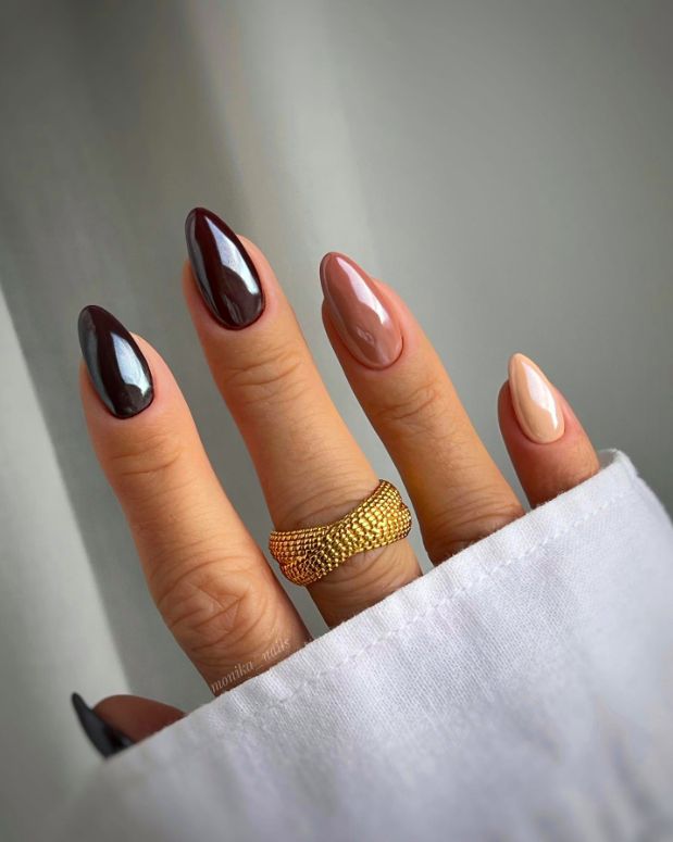 Sophisticated Nail Design: Deep Burgundy and Soft Nude Contrast with Pointed Oval Shape and Gold Ring Accent.