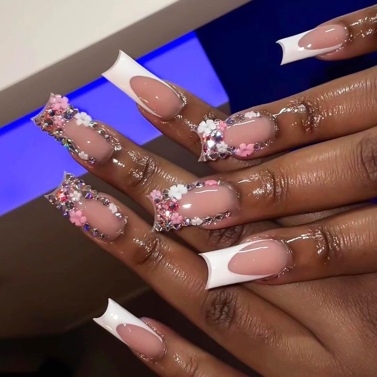 Sophisticated French Manicure with Floral Accents and Colorful Gems on Long Square Tips.