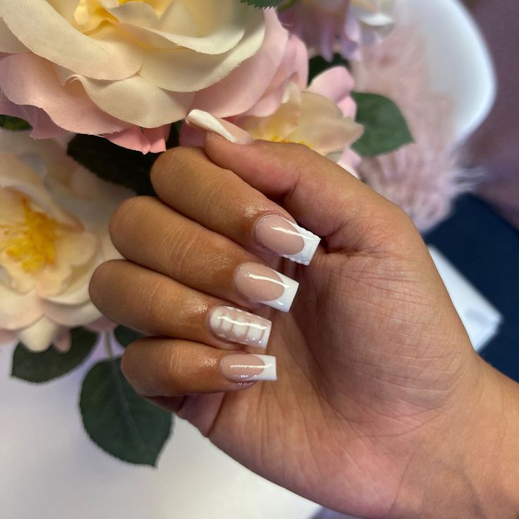 Sophisticated Nude and White French Tip Nails with Unique Embellishments on Floral Backdrop.