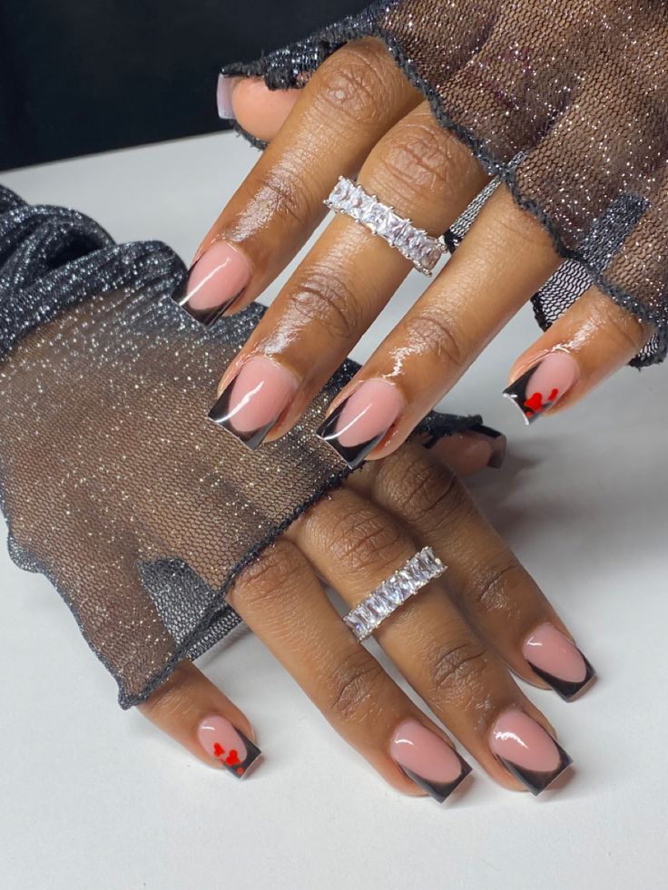 Chic Nude and Black French Manicure with Playful Red Heart Accents and Sparkling Rings.