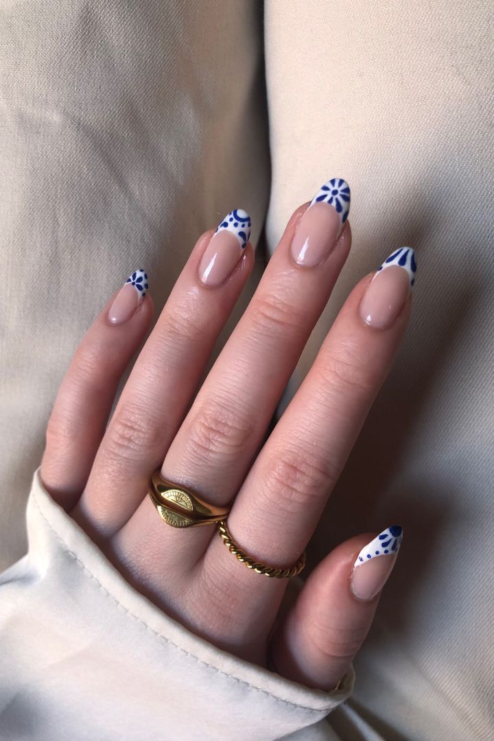 Chic Elegant Nail Design: Soft Nude Base with Vibrant Blue Patterned Tips and Delicate Gold Accents.