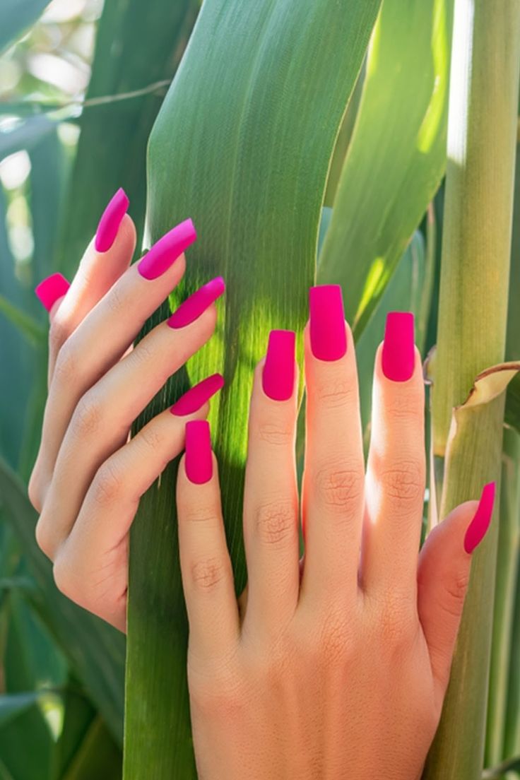 Striking Bold Pink Nails Enhance Creativity Against Lush Greenery.