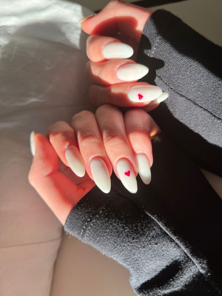 Chic Almond-Shaped White Nails with Red Heart Accents for a Playful, Romantic Look.