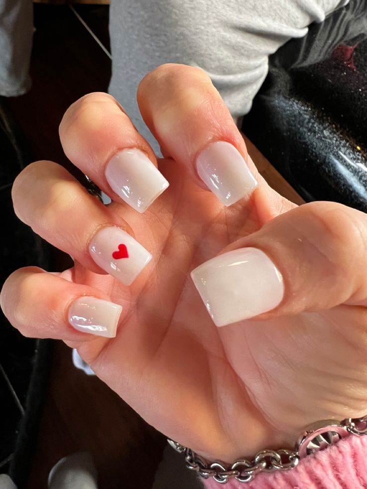 Elegant Nude Nail Design with Whimsical Red Heart Accent.