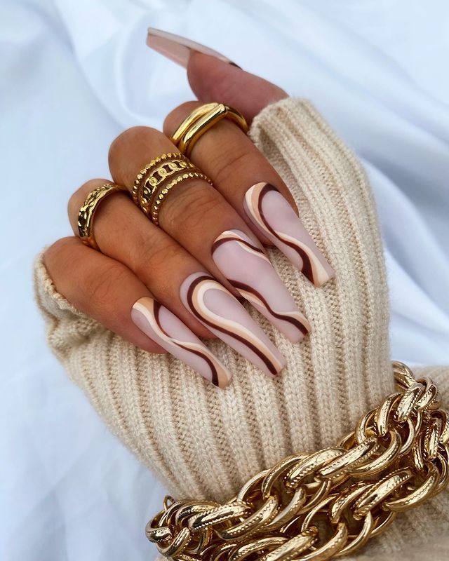 Chic Nail Design: Elegant Nude Tones and Sophisticated Swirls Accentuated by Gold Accessories.