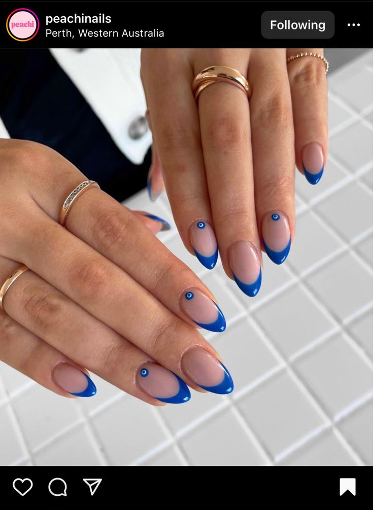 Chic Nail Design: Elegant Nude and Bold Blue French Tips with Gem Accents.