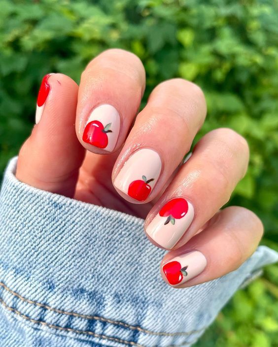 Charming Playful Nail Design with Bright Red Apples on a Soft Nude Base.