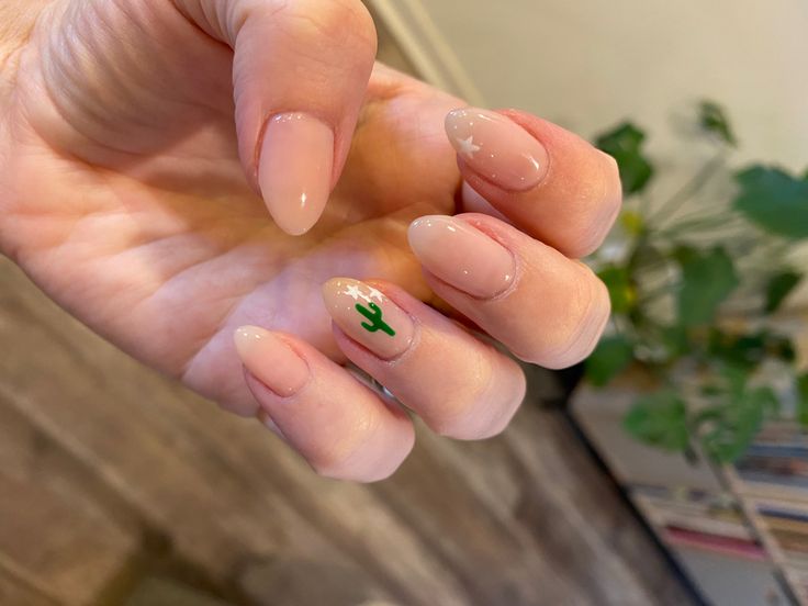 Chic Almond-Shaped Nails with Soft Nude Base, Ombre Effect, and Whimsical Cactus Accent.