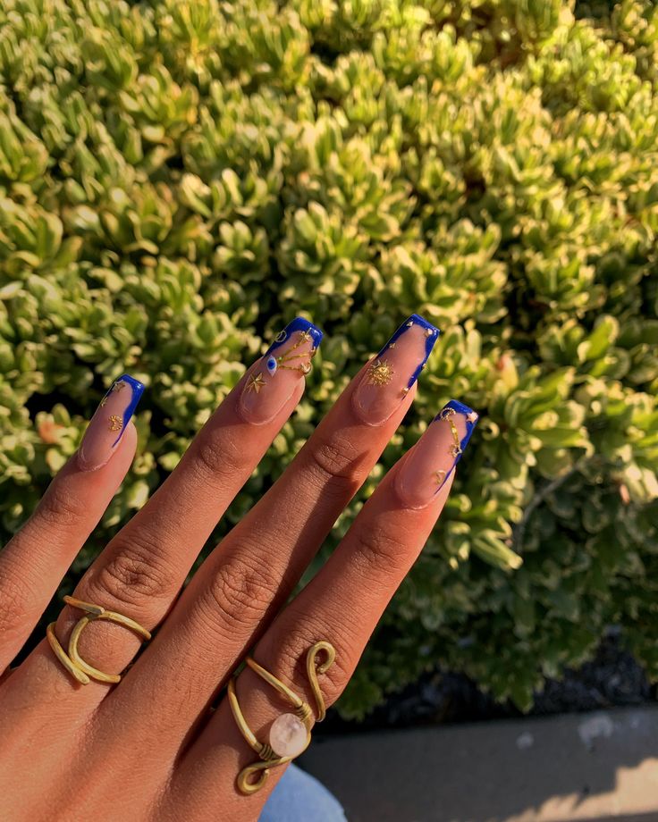 Striking Blue Tip Nail Design with Elegant Gold Floral Patterns and Chic Complementary Rings.