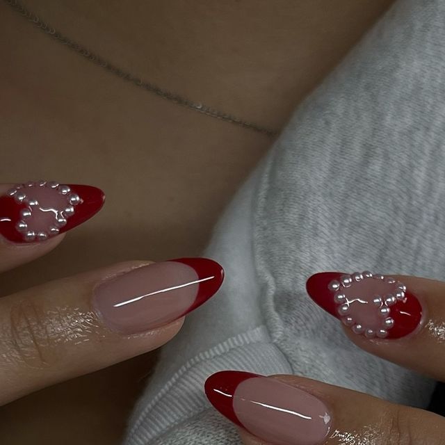 Chic Red French Tip Nail Design with Pearl Accents on Nude Base.