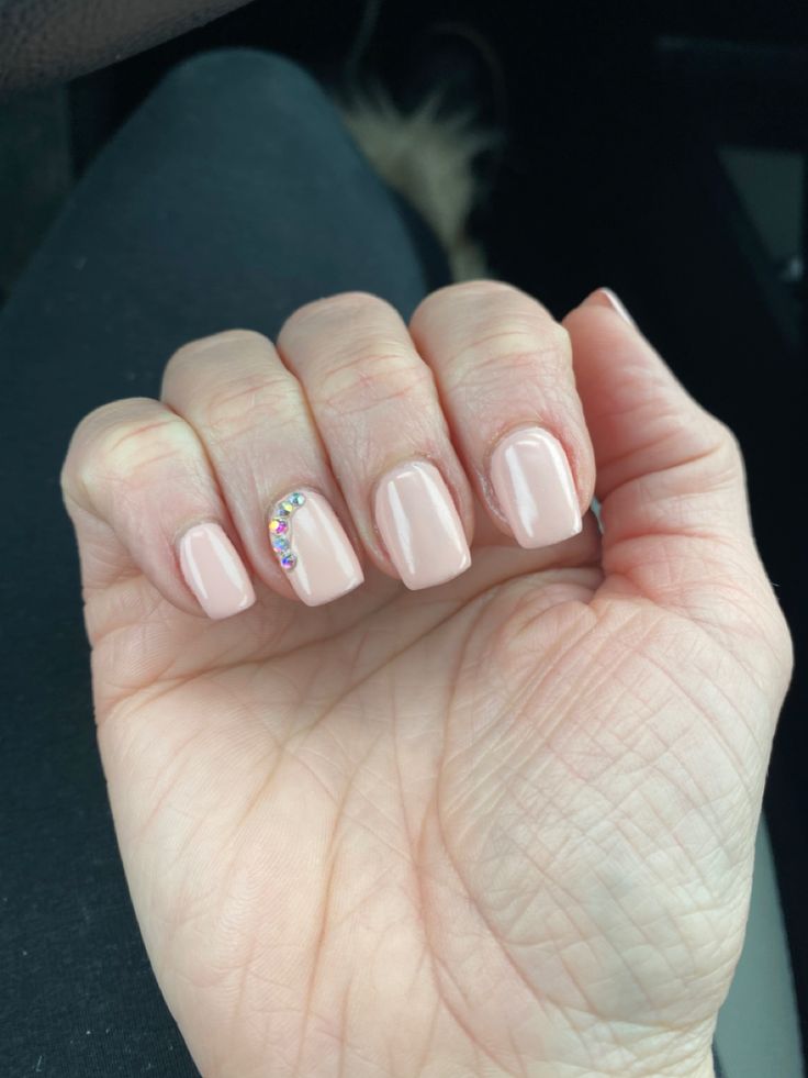 Chic Nude Nail Design with Subtle Shine and Glamorous Gem Accent.