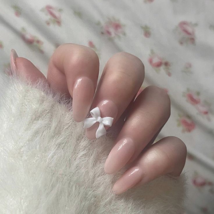 Chic Long Almond Nude Nails with a Sweet White Bow Accent.