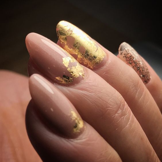 Luxurious Nude and Gold Nail Design with Glitter Accents.