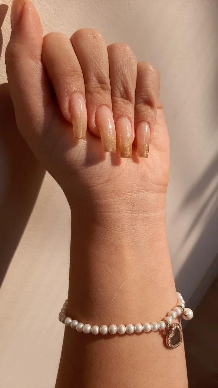 Chic Almond-Shaped Ombre Nails with Golden Glimmer and Heart Charm Bracelet.