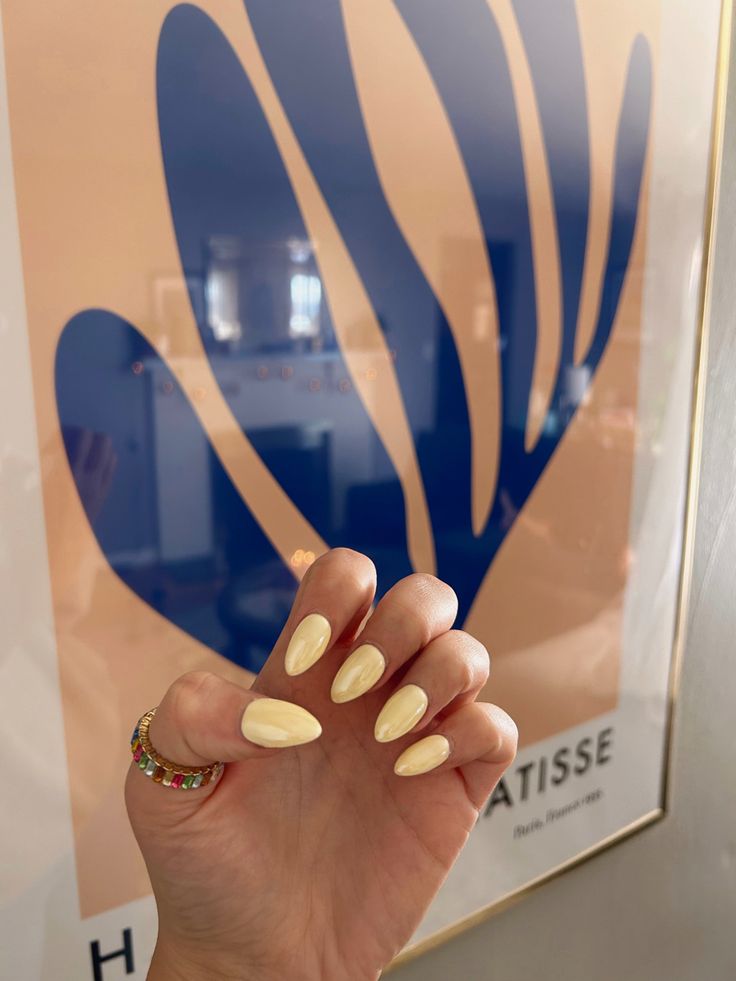 Chic Pastel Yellow Almond-Shaped Nails Enhanced by a Playful Beaded Ring and Minimalist Art Backdrop.