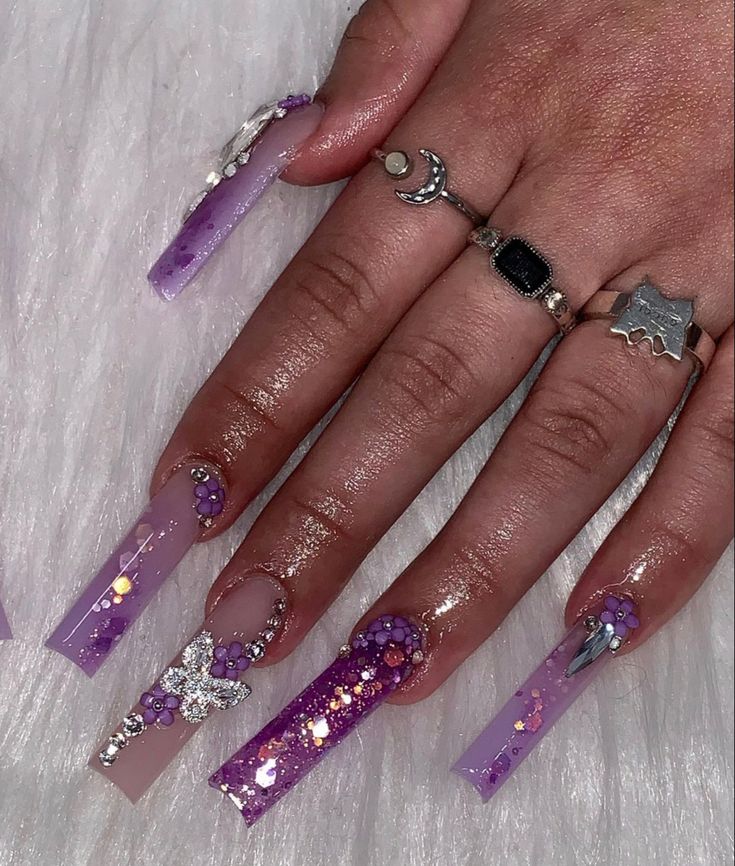 Enchanting Purple Acrylic Nail Art with Glitter, Jewels, and Floral Accents.