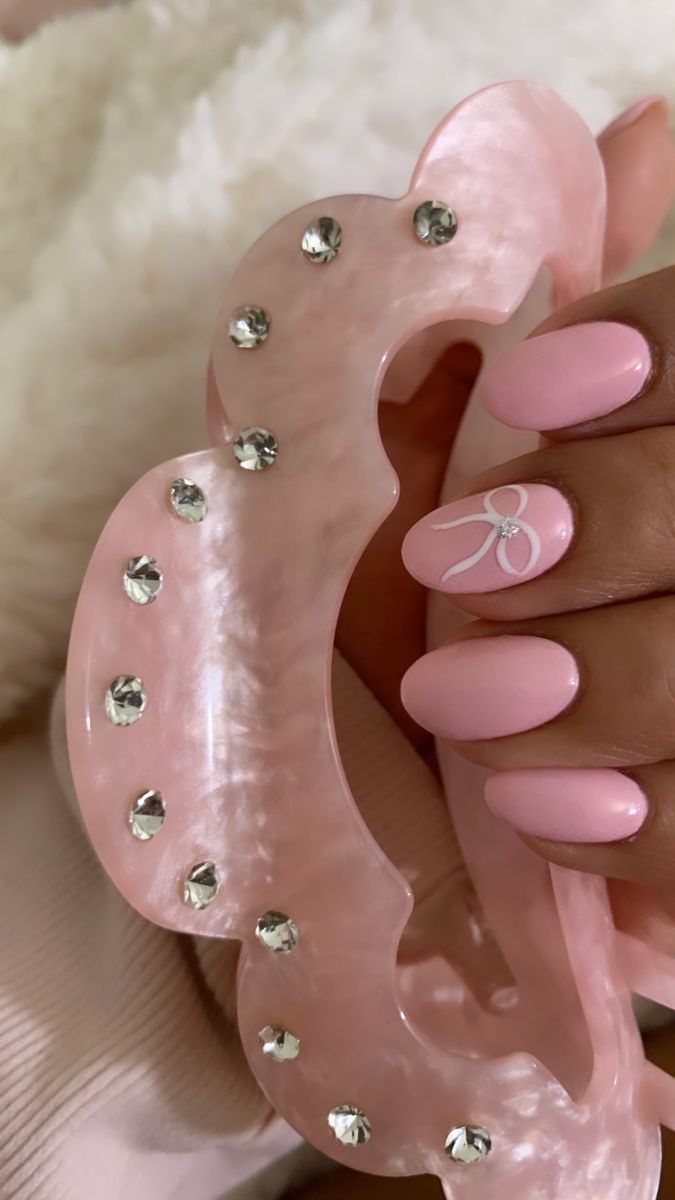 Charming Pastel Pink Nails with Delicate Bow and Sparkling Rhinestones for a Trendy Feminine Look.