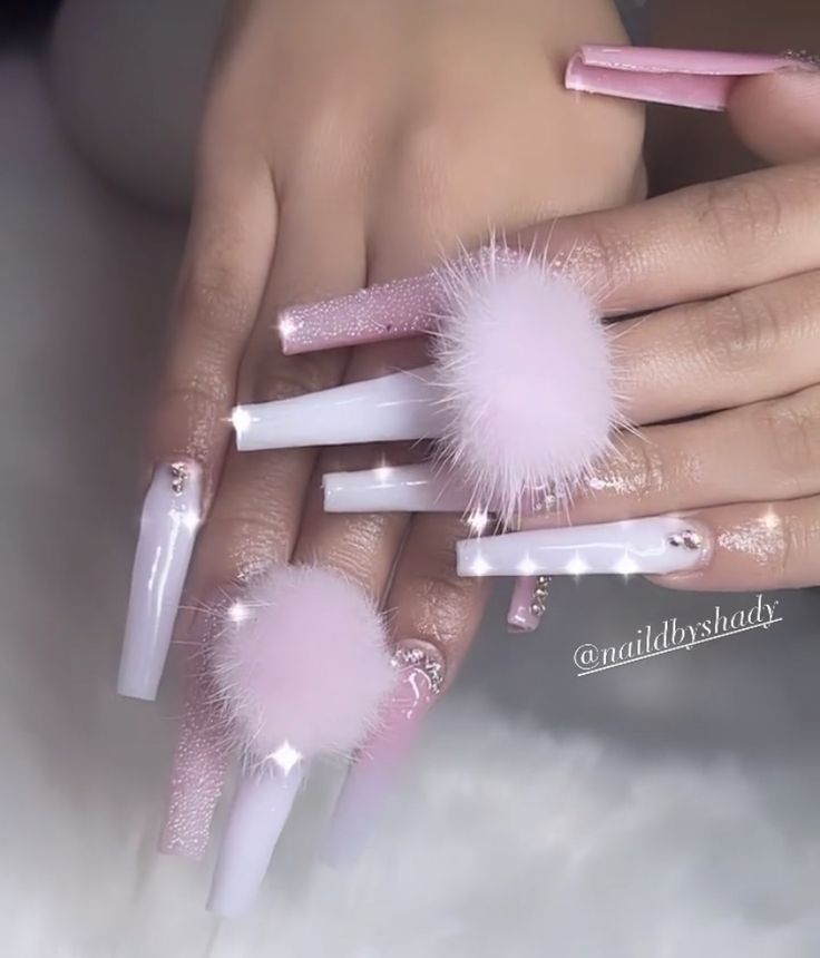 Chic Nail Art: Elongated Acrylic Tips with Playful Pink Pom-Poms and Glitter Accents.