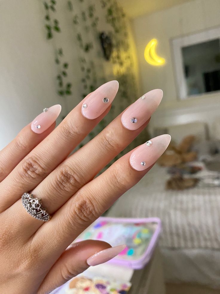 Chic Almond-Shaped Ombre Nails with Rhinestones Set Against a Serene Background.