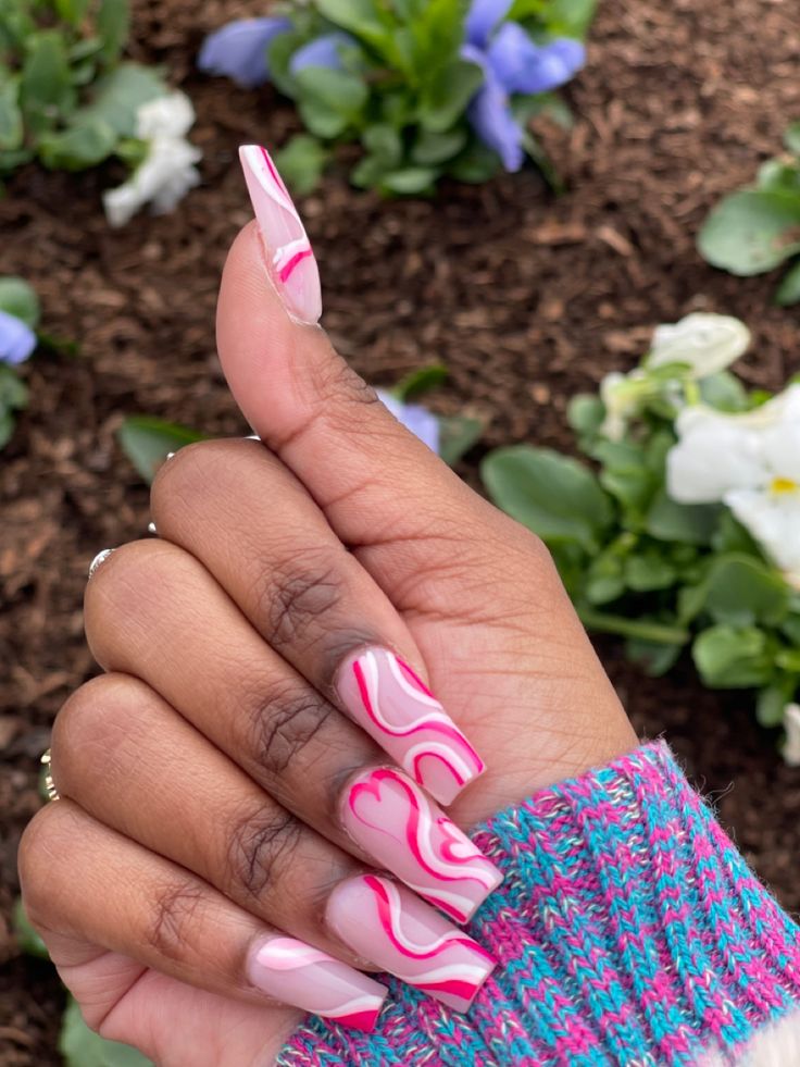 Vibrant Pink and White Marbled Nail Design with Elongated Tips Amidst Blooming Flowers.