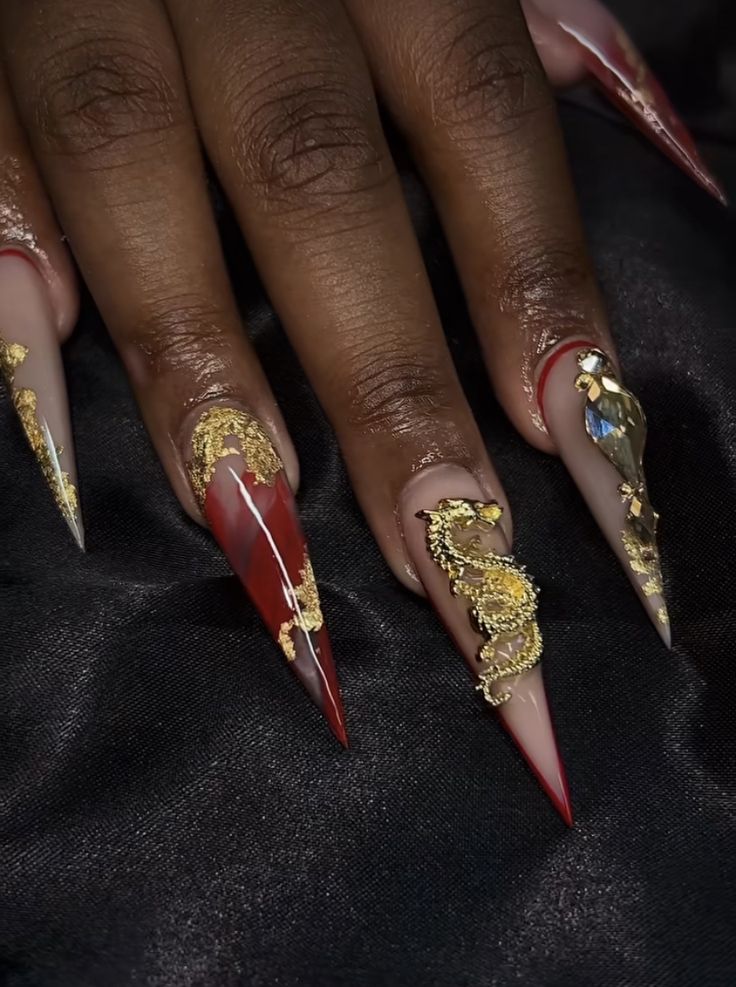 Luxurious Deep Red and Nude Stiletto Nail Design with Gold Detailing and Gems.