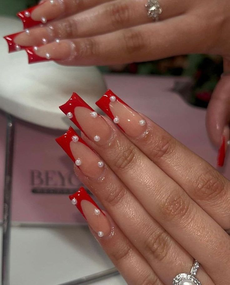 Chic Bold Nail Design: Vibrant Red Accents with Unique Shaped Tips and Elegant Pearls.