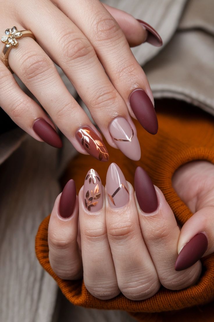 Sophisticated Nail Design: Matte and Glossy Deep Burgundy and Nude with Metallic Accents and Leaf Patterns.